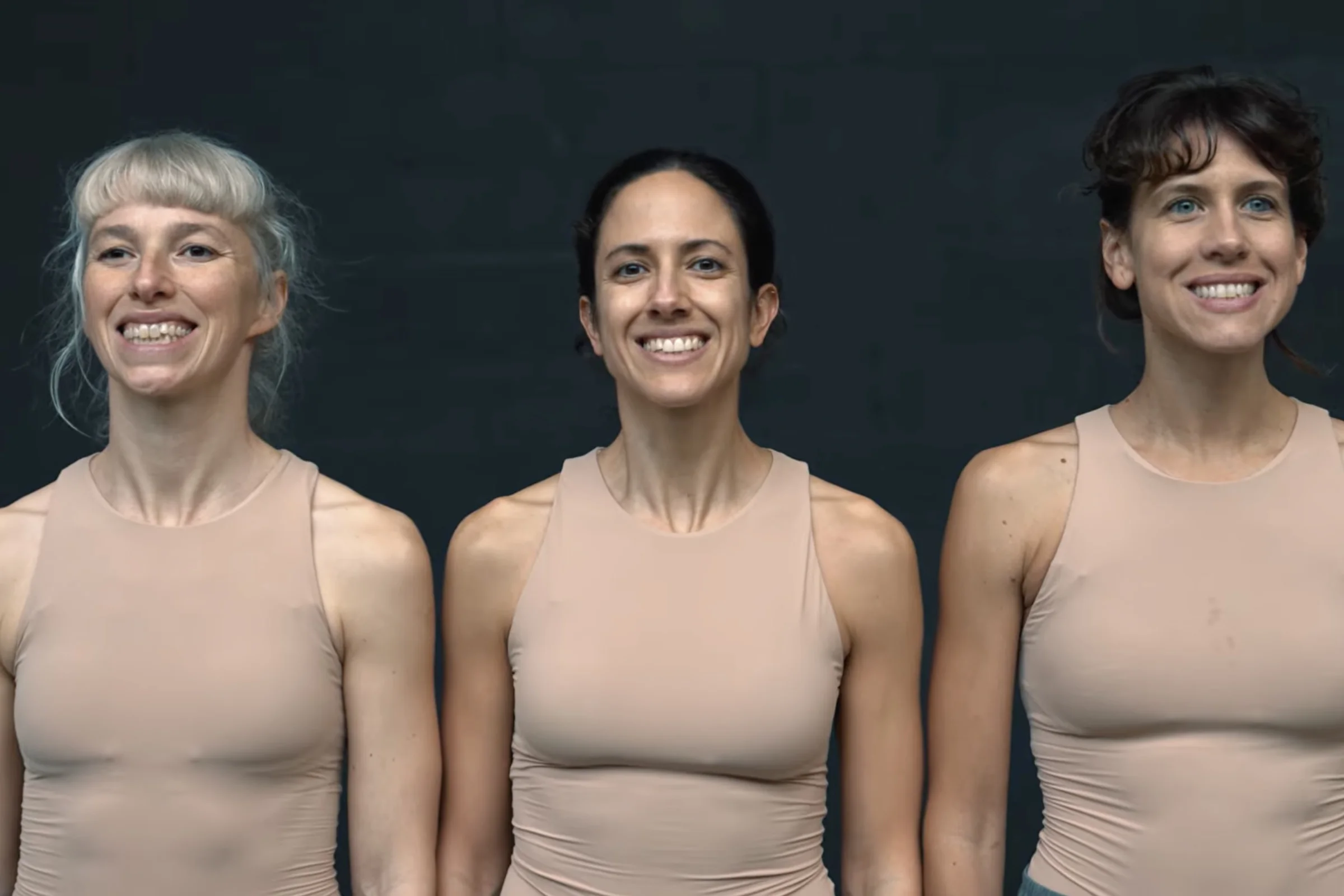 Tres mujeres con una sonrisa forzada. Las tres están de pie y llevan tops sin mangas de color carne.