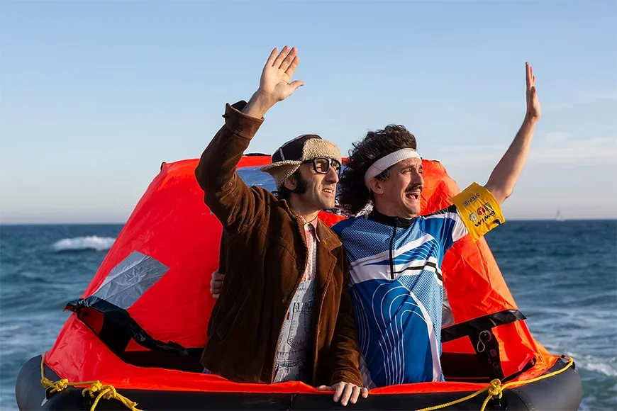 Els dos integrants del dúo Street Fools saluden des d’un bot salvavides enmig del mar.