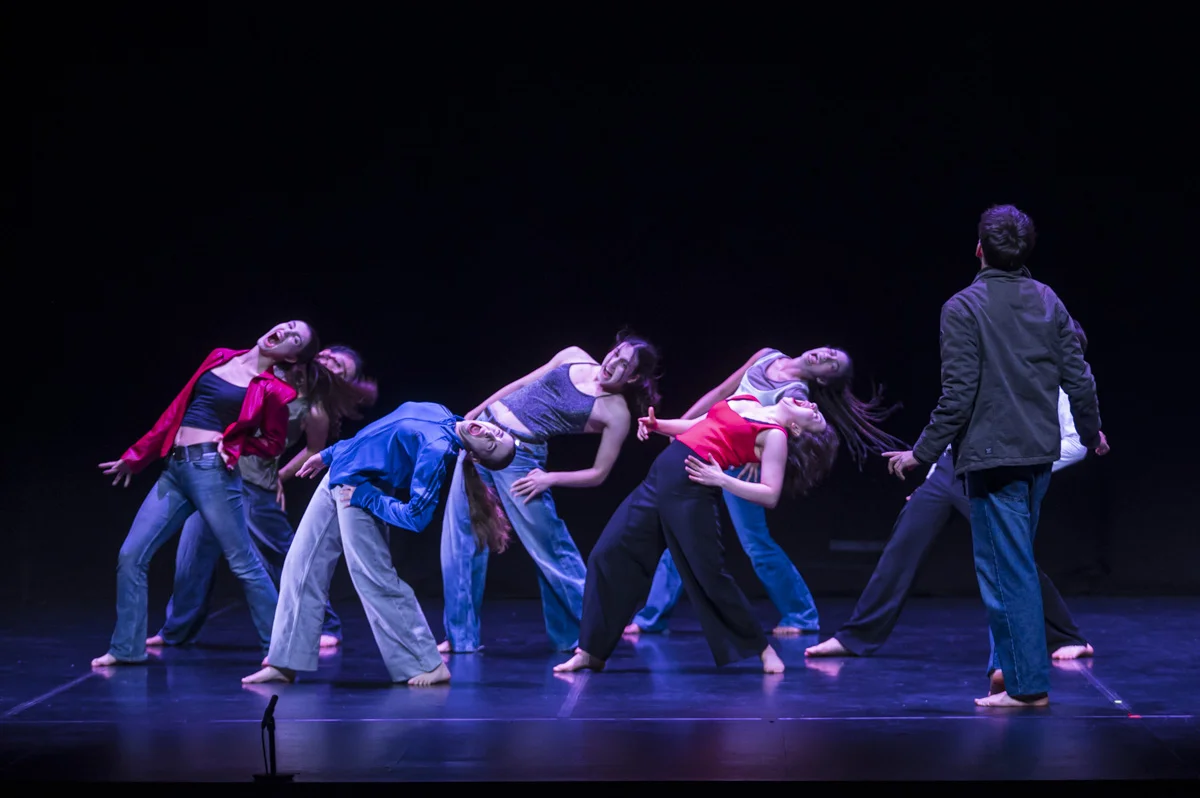 Siete bailarinas realizan una coreografía urbana. Un chico, de espaldas a la cámara, las observa; parece que quiere sumarse a ellas.