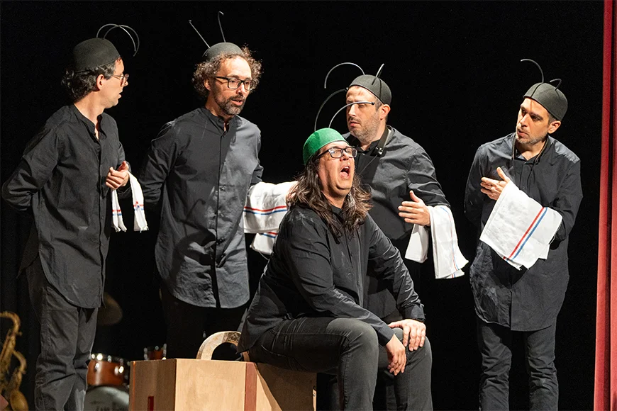 5 actors vestits de negre amb antenes d'insecte al cap.