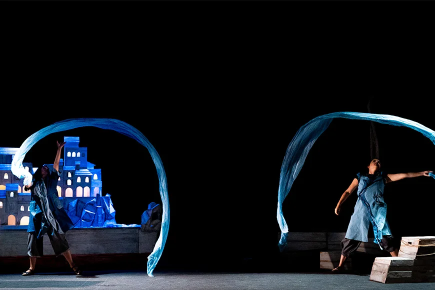 Escena de l’espectacle en què es veuen dos personatges fent girar una tela a l’estil de la cinta de gimnàstica rítmica.