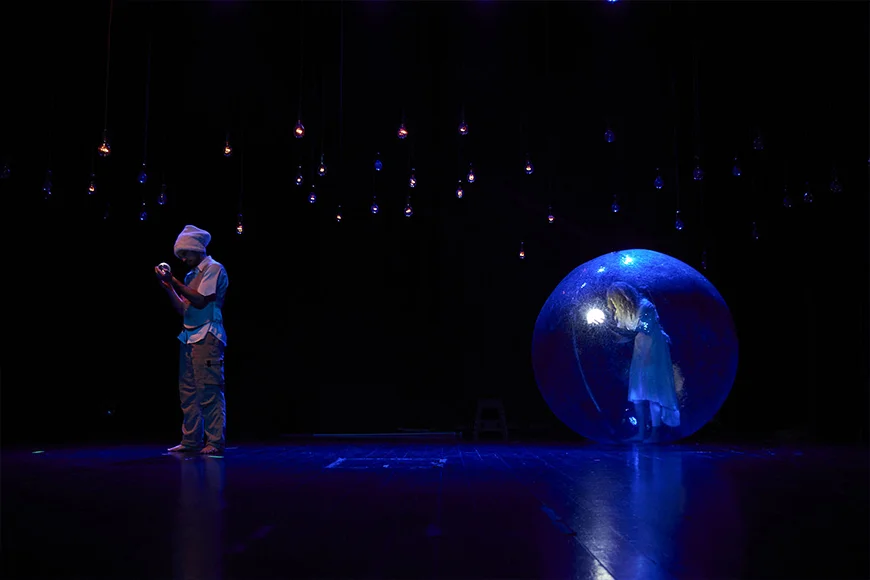 Escena de l’espectacle Nazuri on es veu un personatge mirant una petita bola a les seves mans i un altre personatge dins d’una bombolla gegant.