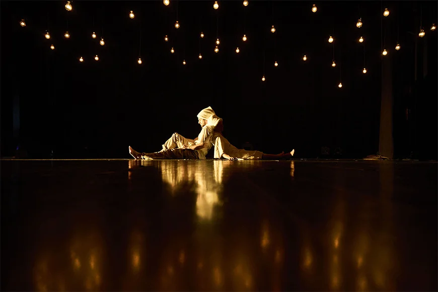 Escena de l’espectacle Nazuri on es veuen dos personatges asseguts a terra, esquena contra esquena.
