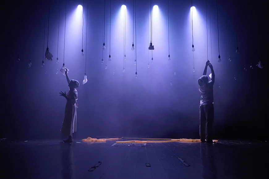 Escena de l’espectacle Nazuri on es veuen dos personatges tocant algunes de les 50 bombetes que pengen de l'escenografia.