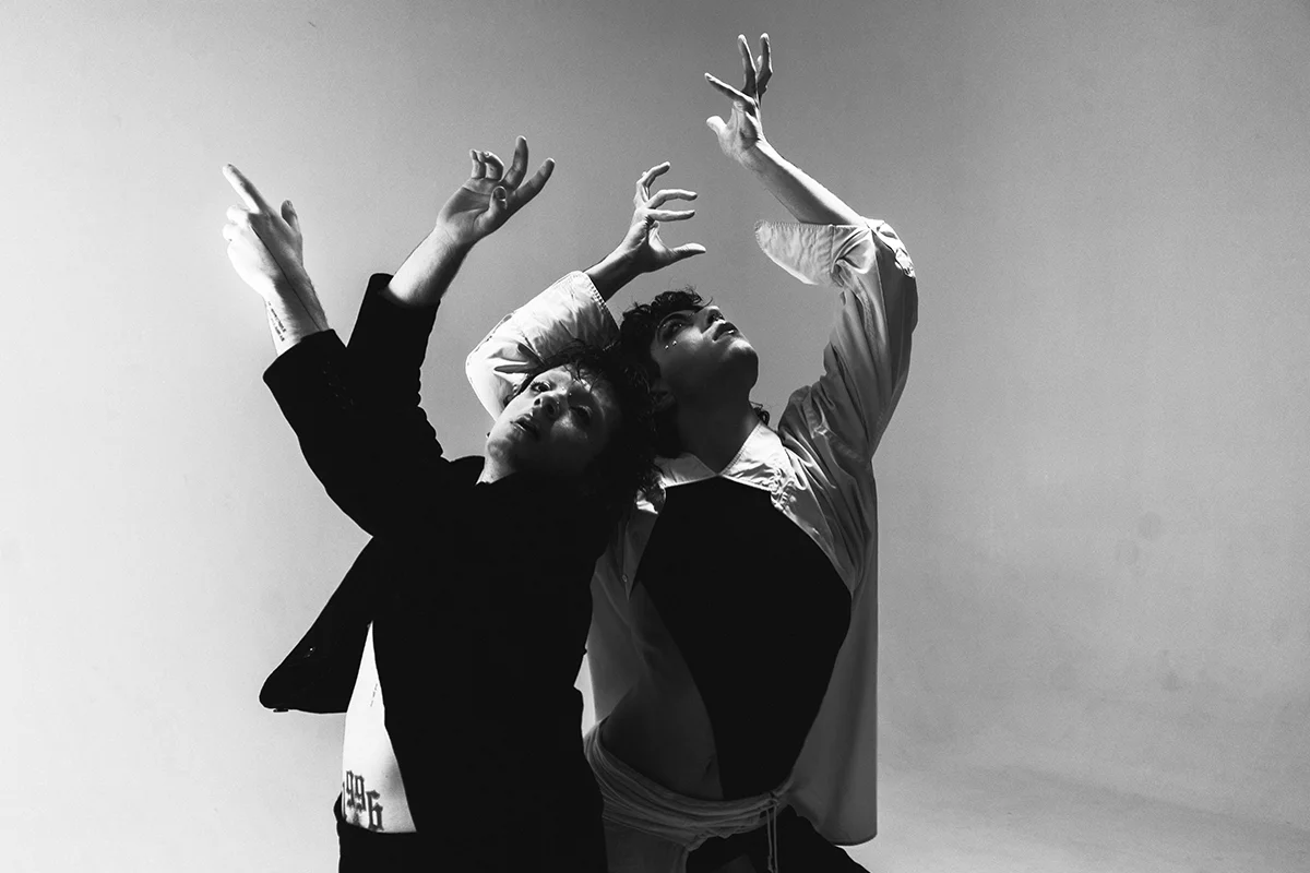 Dos bailarines levantan los brazos en un paso coreográfico. La fotografía es en blanco y negro.