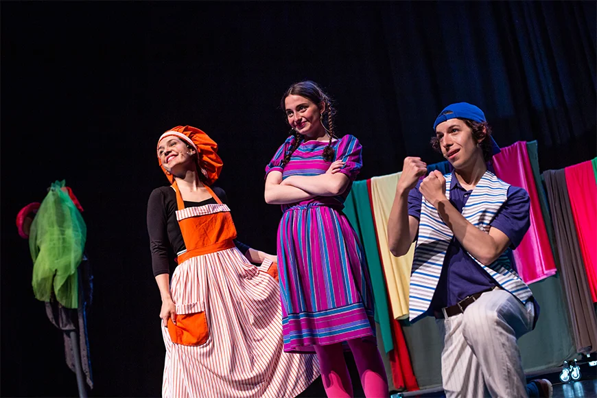 Tres actors somriuen sobre l'escenari. Les dues noies estan dempeus i el noi està agenollat ??i mostrant els punys.